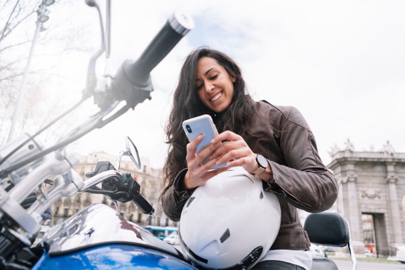 woman smiling and using her phone sitting on a motorcycle