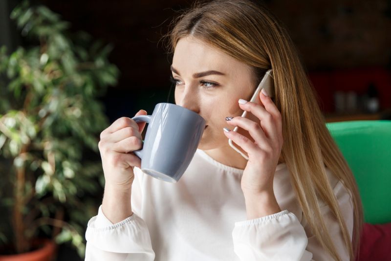 young woman making a phone call while drinking a cup of coffee