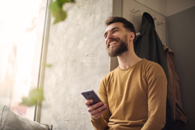 Young man passionately smiling while using his phone in his room