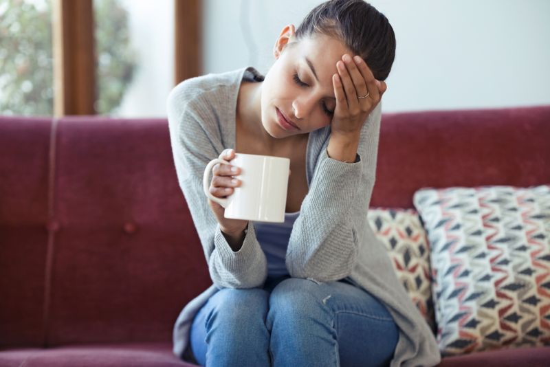 Overwhelmed woman holding a coffee mug with her head in her hand