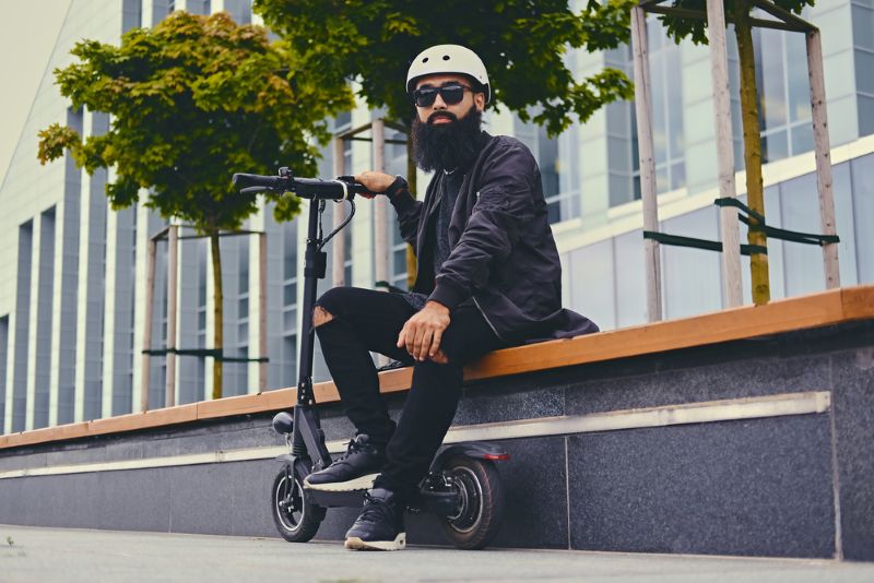 Man wearing a helmet and sitting outside with scooter